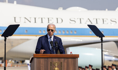 Joe Biden in sunglasses stands at a speaker's podium before Airforce 1