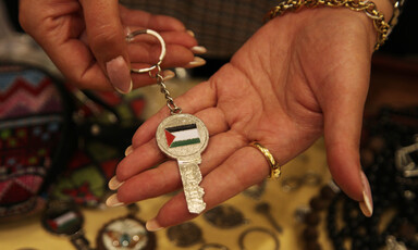 A woman holds a key bearing the Palestinian flag in her hand