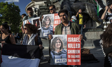 People hold posters reading "Israel killed Shireen to silence the truth" while standing in front of statue