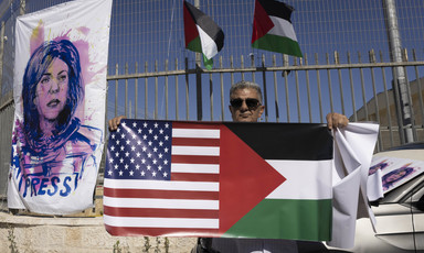 Person holds a banner with the US and Palestinian flags side by side next to a poster showing an illustration of Shireen Abu Akleh