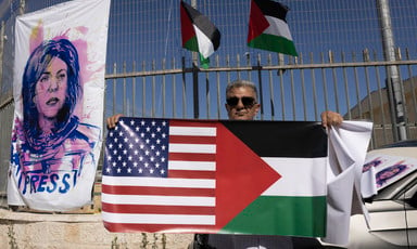Person holds a banner with the US and Palestinian flags side by side next to a poster showing an illustration of Shireen Abu Akleh