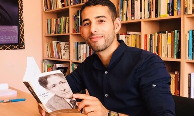 Mosab Abu Toha sits at a table in the Edward Said Library holding a book