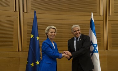 Man and woman clasp hands in front of EU and Israeli flags
