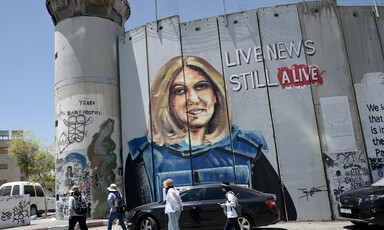 People walk past a mural of Shireen Abu Akleh wearing a press vest on Israel's militarized wall in the West Bank