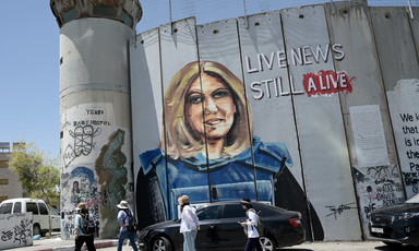 People walk past a mural of Shireen Abu Akleh wearing a press vest on Israel's militarized wall in the West Bank