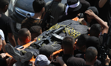 Men carry a flag-wrapped body on a stretcher with a weapon on top 