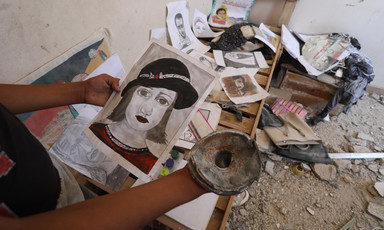 A portrait of a woman wearing a hat is held by a hand while some other pictures are laid out on a wooden bed