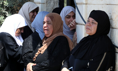 Women cry while standing outside home