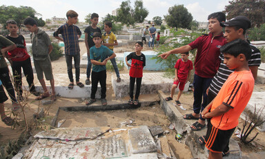 Children stand around a shattered gravestone