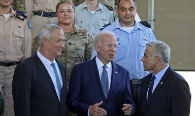 Three men in suits stand in front of military personnel