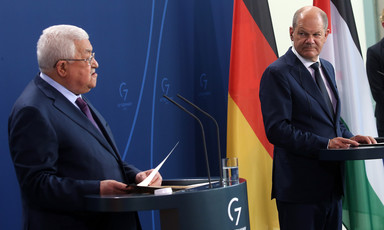 Two men stand at podiums with German and Palestinian flags