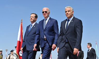 Joe Biden, wearing sunglasses, walks with Isaac Herzog to his right and Yair Lapid to his left