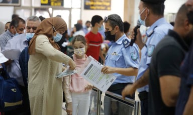 Officer holds paper while standing next to woman and young girl with other travelers in the background 