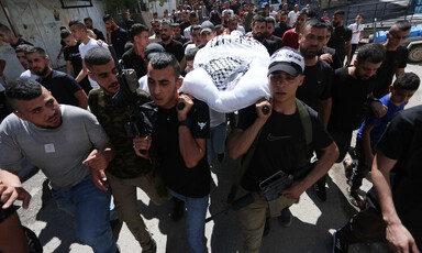 Armed men carry a stretcher bearing a body