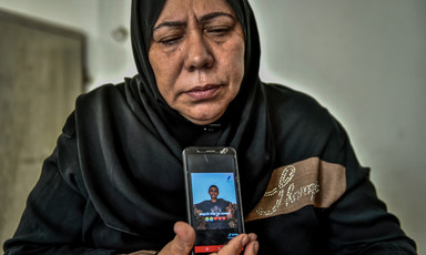 Woman with closed eyes and wearing black headscarf holds a mobile phone showing photo of young man