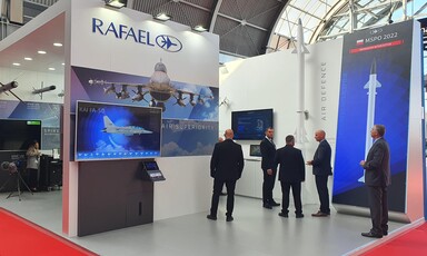 Men wearing suits stand beside large images depicting planes and missiles