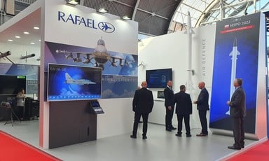 Men wearing suits stand beside large images depicting planes and missiles