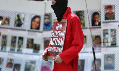 A masked man with a poster stands in front of pictures of children slain in Gaza