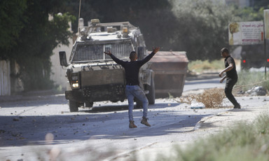 Young man with his  arms in the air stands in front of military vehicle