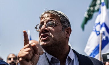 A man points with an Israeli flag behind him