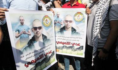 People hold two identical posters side by side showing the face of a bald man wearing sunglasses 