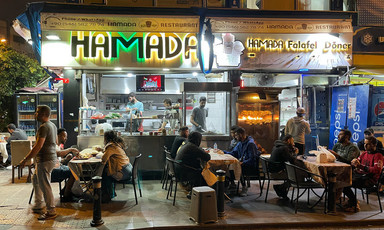 People sit at tables on sidewalk in front of diner at night