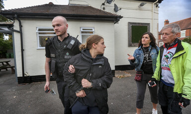 A police officer takes away a handcuffed woman, turning to speak to two others behind her