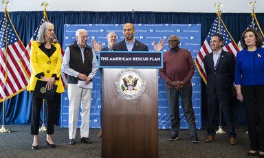 Man speaks from podium with several people looking on