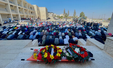 People pray before someone's corpse on a stretcher adorned with flowers 