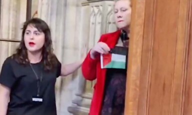 One woman places her hand on the plinth of a statue while another woman holds a small flag