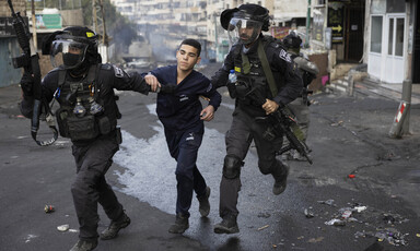 Two police officers grab a boy on each of his arms 