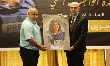 Two men hold framed picture of Shireen Abu Akleh while standing on stage