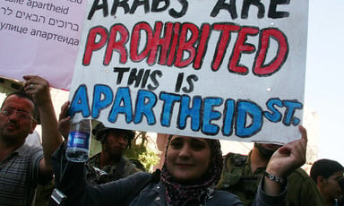 A young woman holds a sign reading in English: Arabs are prohibited This is apartheid"