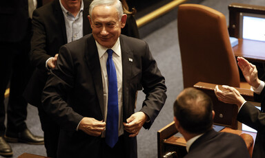 Benjamin Netanyahu smiles while walking and surrounded by other people in suits