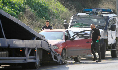 Two men, one wearing police uniform, load a car onto a tow truck with police vehicle behind them