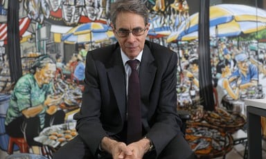 Kenneth Roth, wearing a suit, sits in front of a mural of a lively street scene