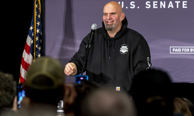 Man wearing a hoodie stands beside flag with stars and stripes 