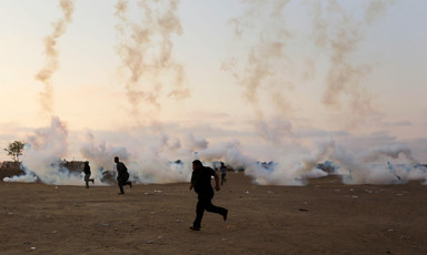 Clouds of tear gas smoke rise from canisters on the ground as a group of Palestinian men run for safety