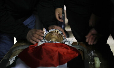 Hands caress the face of a dead boy wrapped in a scarf and flag 