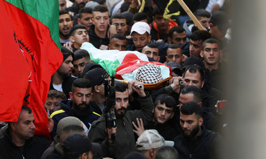 Men carry the coffin of a boy wrapped in a flag, some of them carrying rifles 