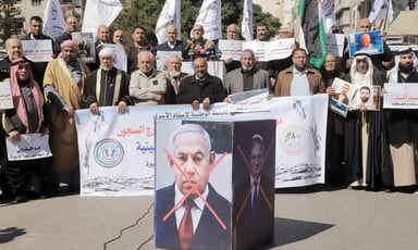 People hold signs, flags and banners and display images of Israeli officials with their faces crossed out