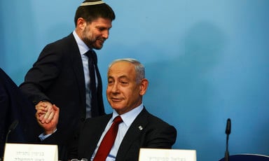 Bezalel Smotrich grasps a seated Benjamin Netanyahu's hand while they both smirk