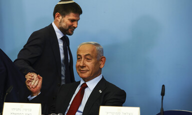 Bezalel Smotrich grasps a seated Benjamin Netanyahu's hand while they both smirk