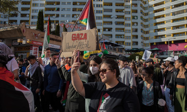 People march in a busy street with Palestinian flags and signs
