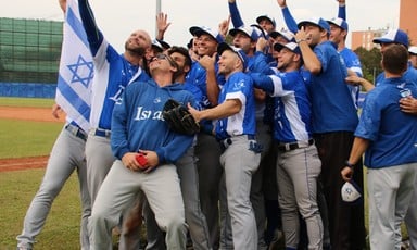 Members of the Israeli baseball team pose for selfies beside a flag 