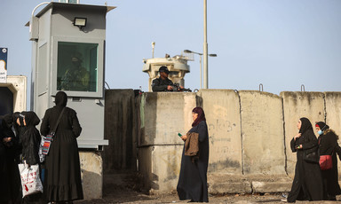 Woman walk in front of concrete barriers with armed Israeli soldiers standing above them