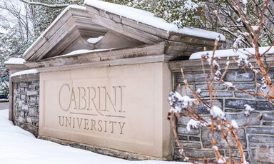Snow and bushes surround a stone sign with the name of the university