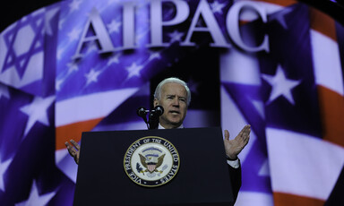 Joe Biden speaks before screen showing AIPAC's name and American and Israeli flags