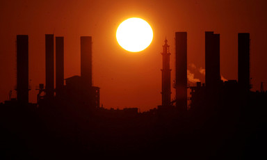 A giant yellow sun sets over the silhouette of a Gaza power station