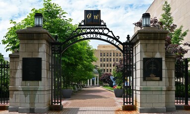 A gate in the campus of George Washington University arcs between two concrete pillars.